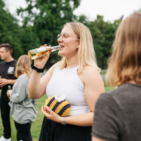 Kathi von Limoment trinkt eine Limoment Apfel-Minze Naturlimo und hält dabei Bimo, das Bienen-Maskottchen, in der Hand.