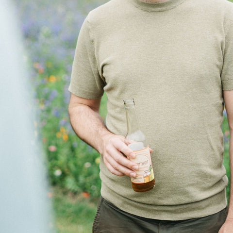Ein Mann im grünen T-Shirt hält eine Flasche Limoment Birne-Grüntee natürlicher Eistee in der Hand vor seinem Körper.
