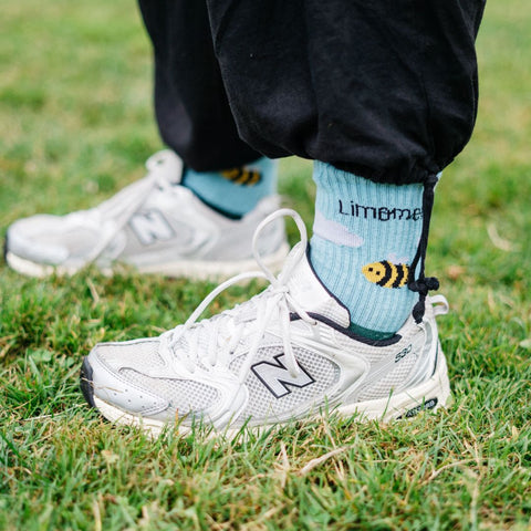 Eine Person mit weißen Schuhen steht auf einer Wiese und trägt die Summsocken von Limoment.
