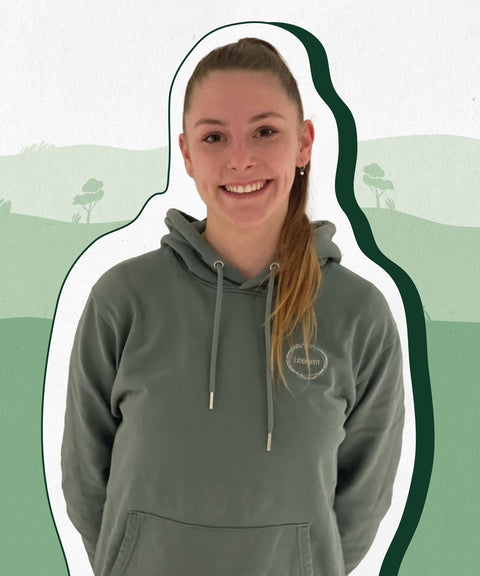 Limoment Teammitglied Katha hat einen Zopf mit langen brauen Haaren, braune Augen, trägt einen grünen Pullover und lächelt.
