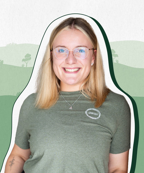 Limoment Teammitglied Kathi hat mittellange blonde Haare, eine Brille, braune Augen, trägt ein grünes T-Shirt und lächelt.