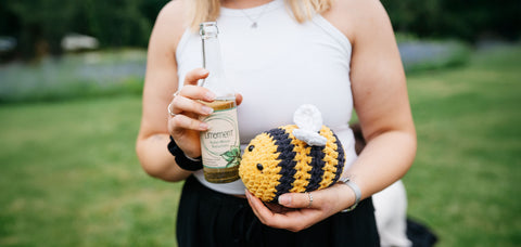 Eine Frau hält eine Flasche Limoment Apfel-Minze Naturlimo und ein Bienen-Stofftier Bimo, das Maskottchen von Limoment, vor ihrer Brust.